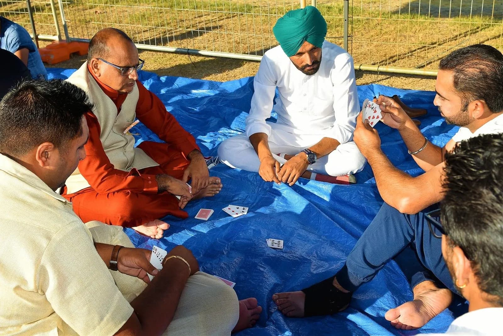 Men sit on a tarp playing a game of cards (taash) at the mela